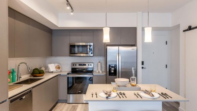 The Upland Modern kitchen with gray cabinets, stainless steel appliances, and a small island with two stools and tableware.