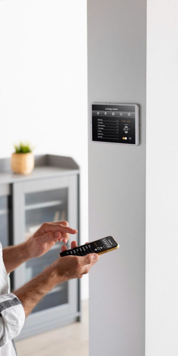 The Upland Man using a smartphone to control a smart home panel on a white wall in a modern living space.