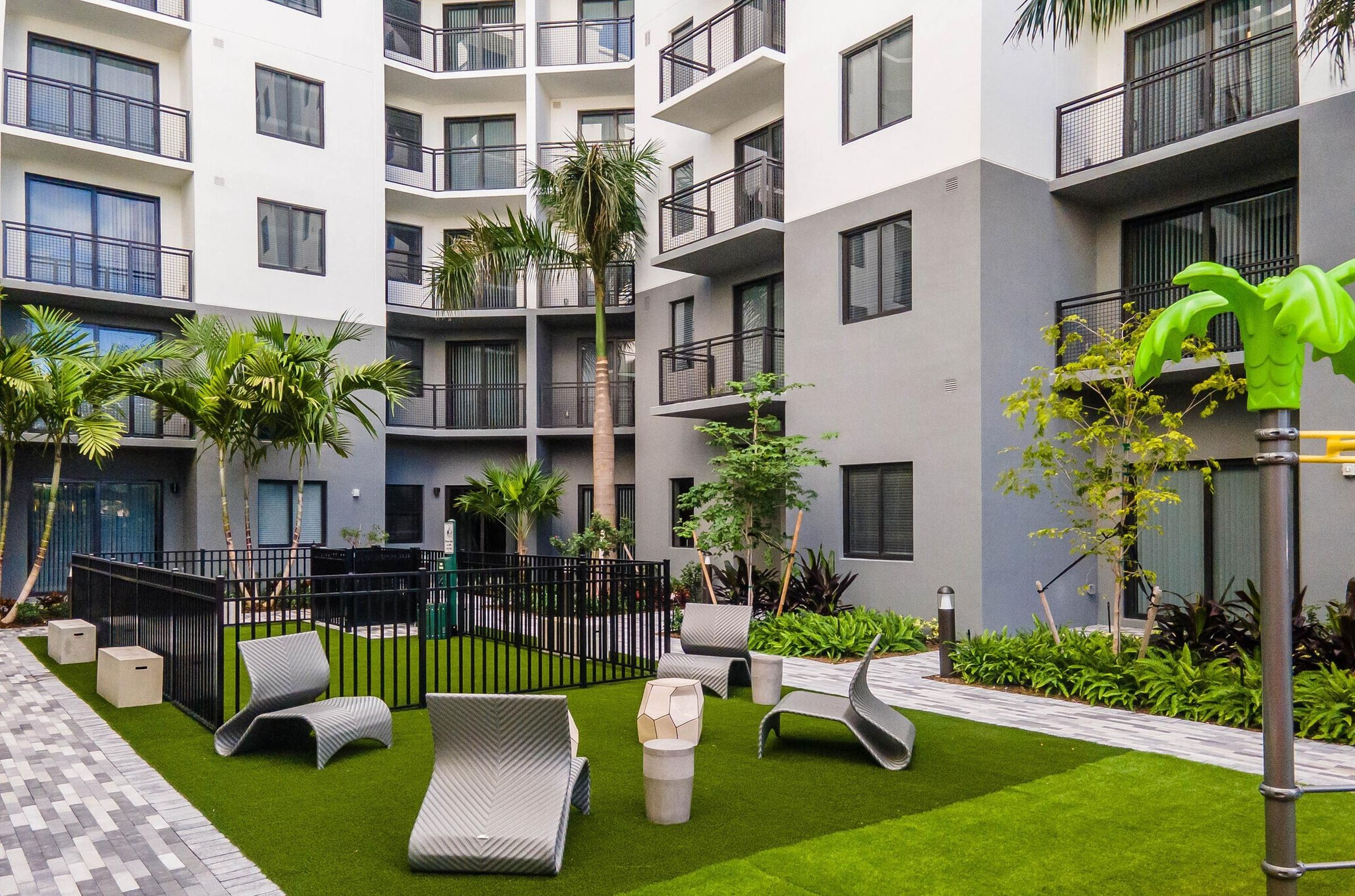 The Upland Modern apartment courtyard with lounge chairs, greenery, and a small playground on artificial grass.
