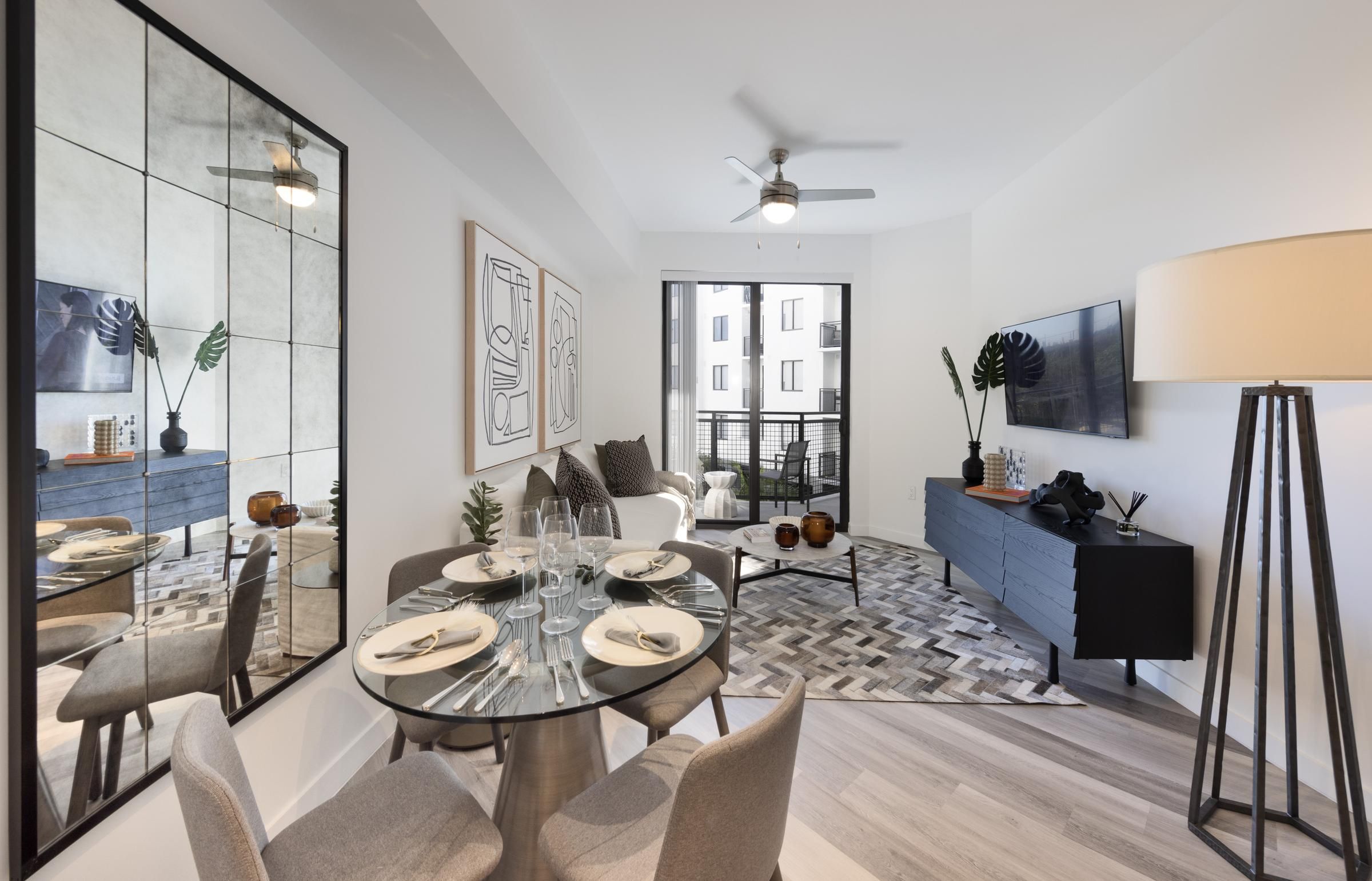 The Upland Modern living and dining area with a round table, chairs, large mirror, artwork, and a balcony view.