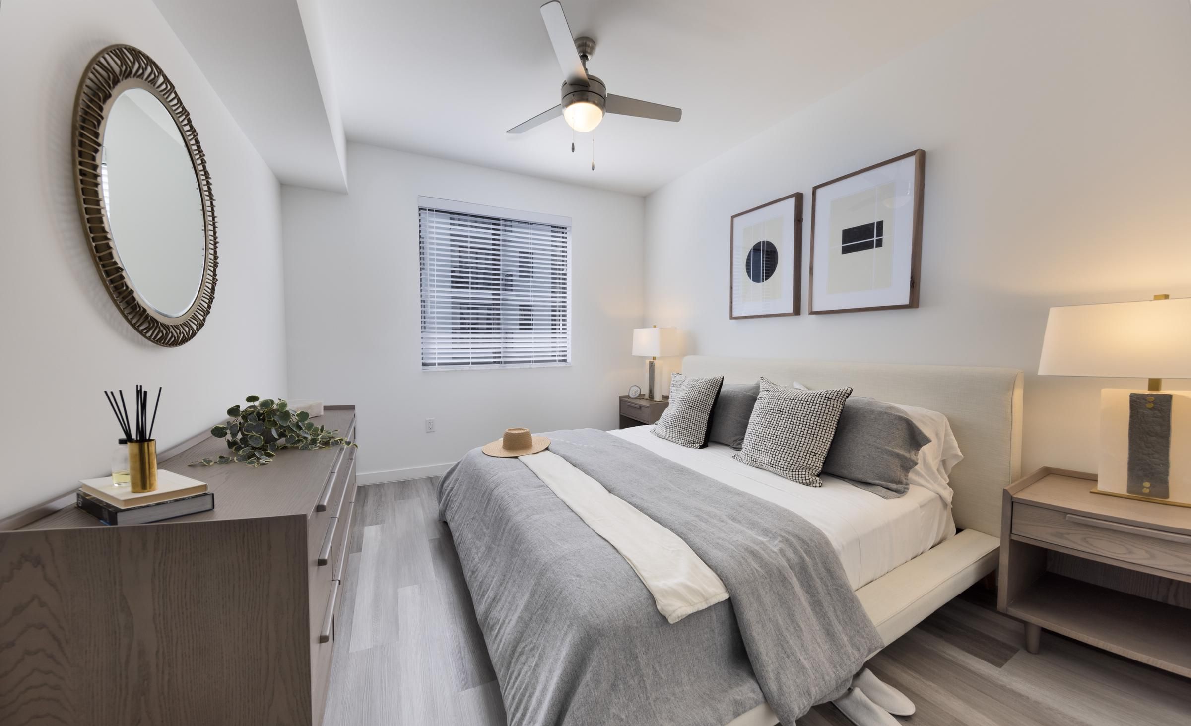 The Upland Modern bedroom with a neatly made bed, two framed artworks, a ceiling fan, and a dresser with a round mirror.