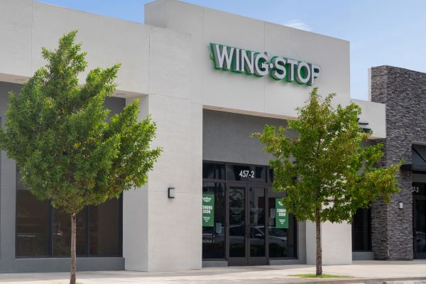 The Upland Exterior of a Wingstop restaurant with white facade and green signage, flanked by trees and a neighboring building.