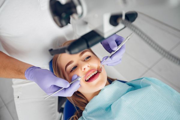 The Upland Person smiling during a dental check-up, with dentist's hands in purple gloves using dental tools.
