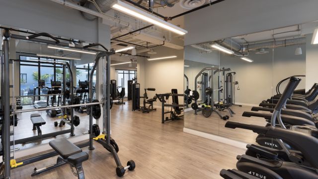 The Upland Modern gym with exercise machines, free weights, and mirrored walls on light wood flooring.