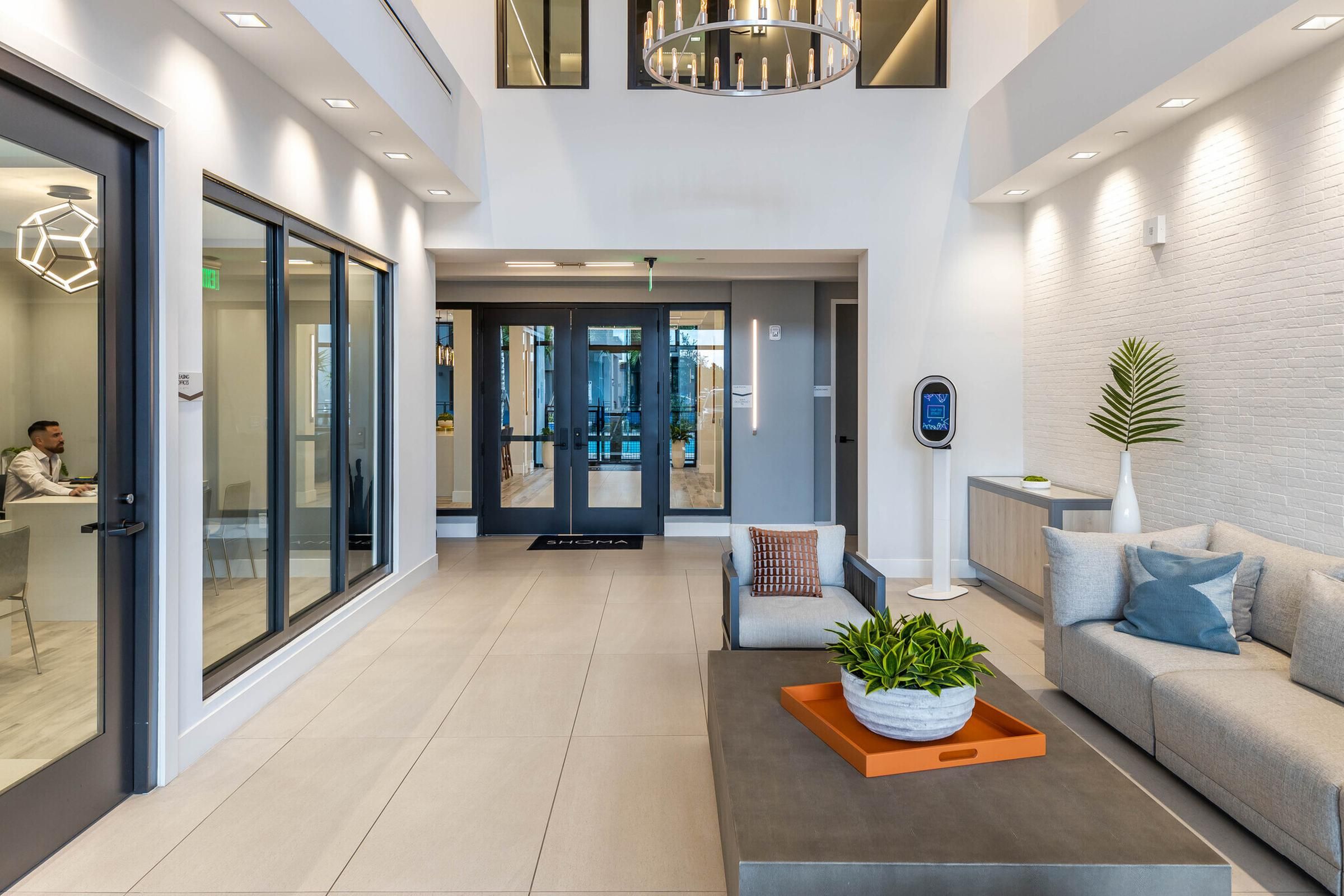 The Upland Modern office lobby with a gray couch, plants, and glass doors. A person is sitting inside a meeting room on the left.