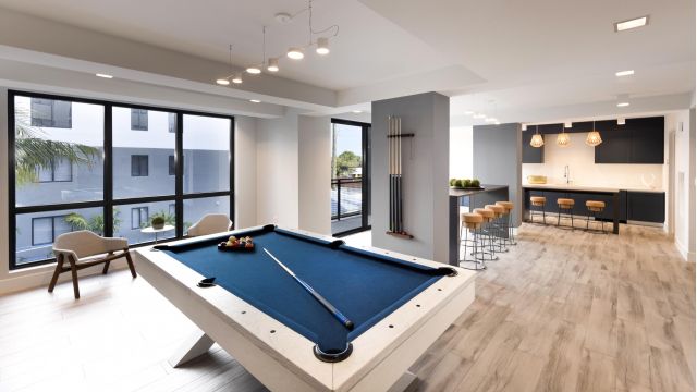 The Upland Modern room with a blue pool table, bar counter with stools, minimalist decor, and large windows.