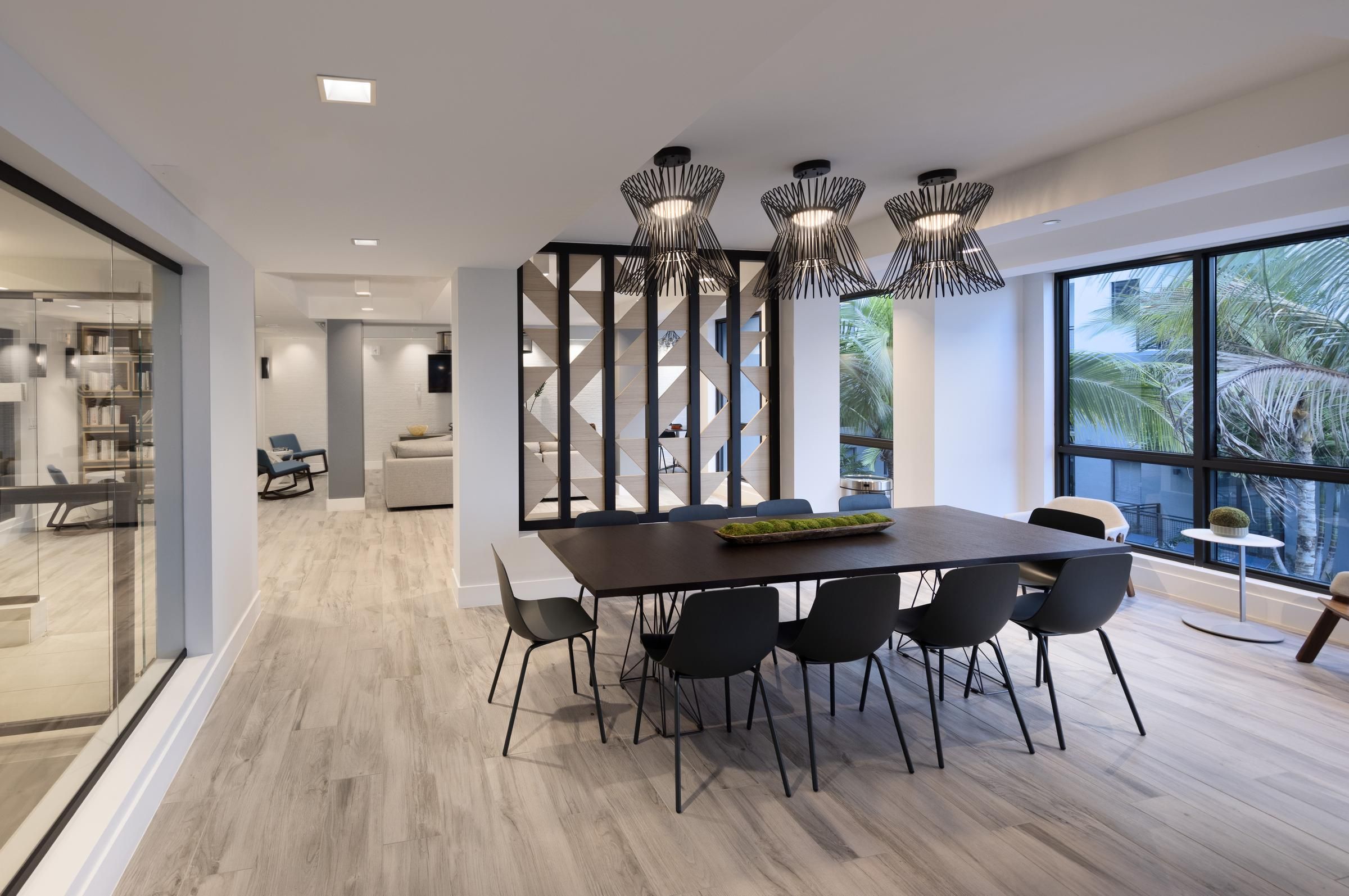 The Upland Modern dining area with a long table, black chairs, and geometric lights, large windows showing palm trees outside.
