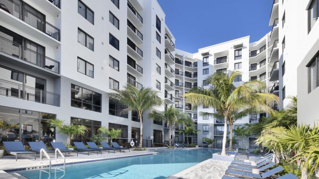 The Upland Modern apartment building with a courtyard pool, surrounded by lounge chairs and palm trees.