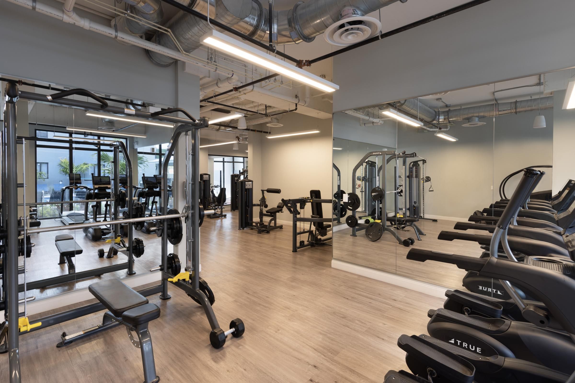 The Upland Modern gym with exercise machines, free weights, and mirrored walls on light wood flooring.